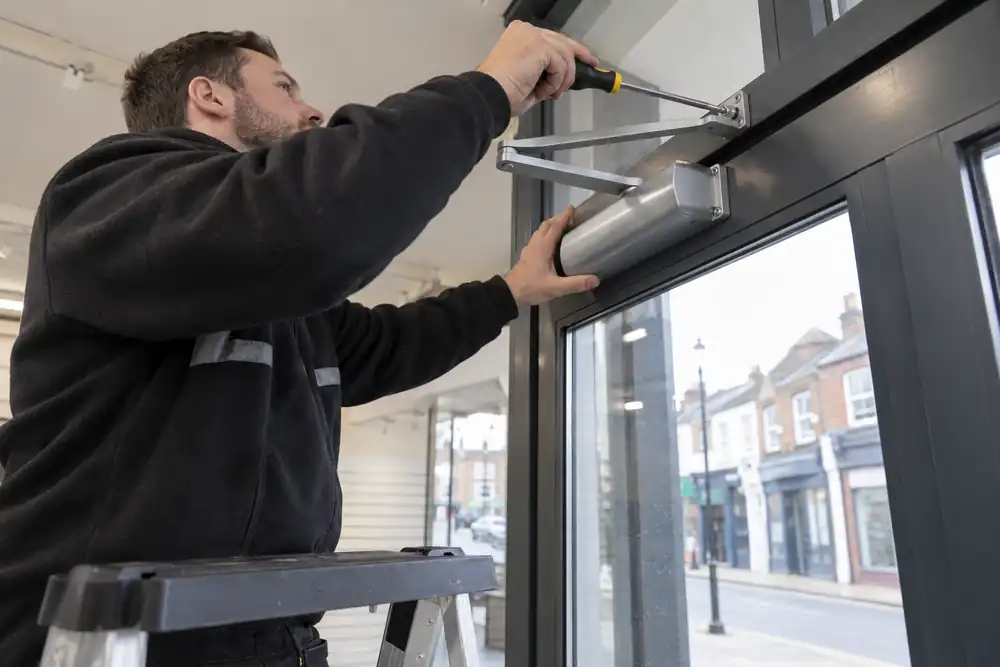 Technician fitting an overhead closer to a glazed shop door