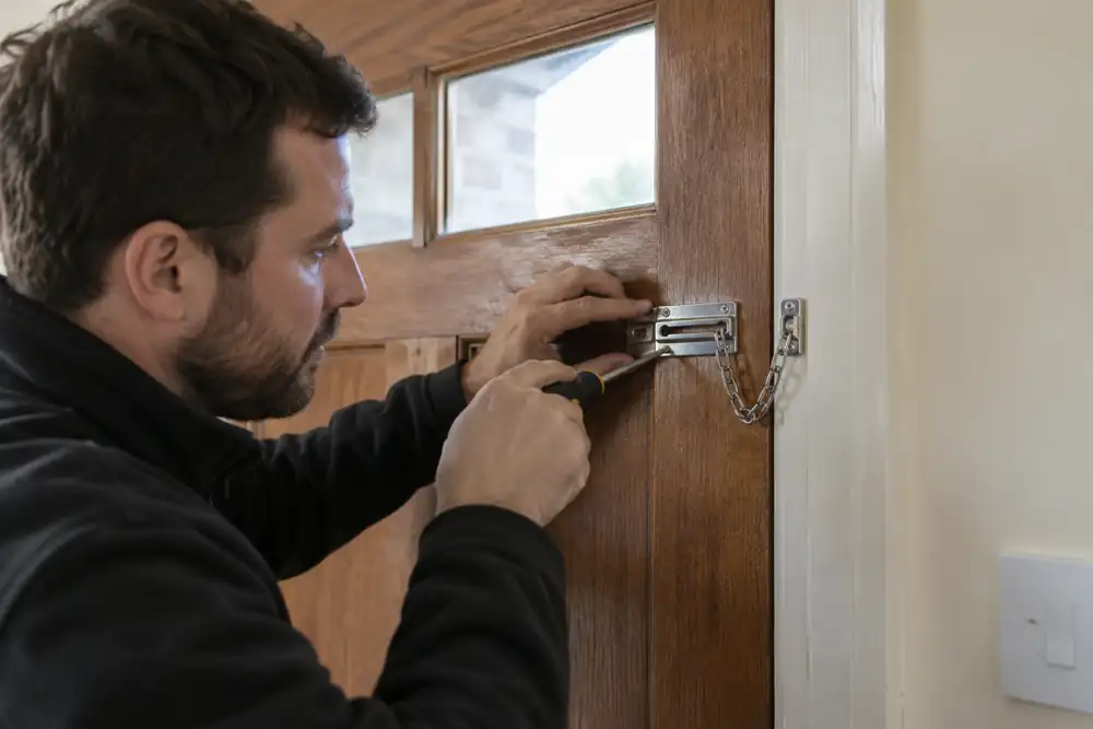 Locksmith fitting a door chain to a timber front door interior.